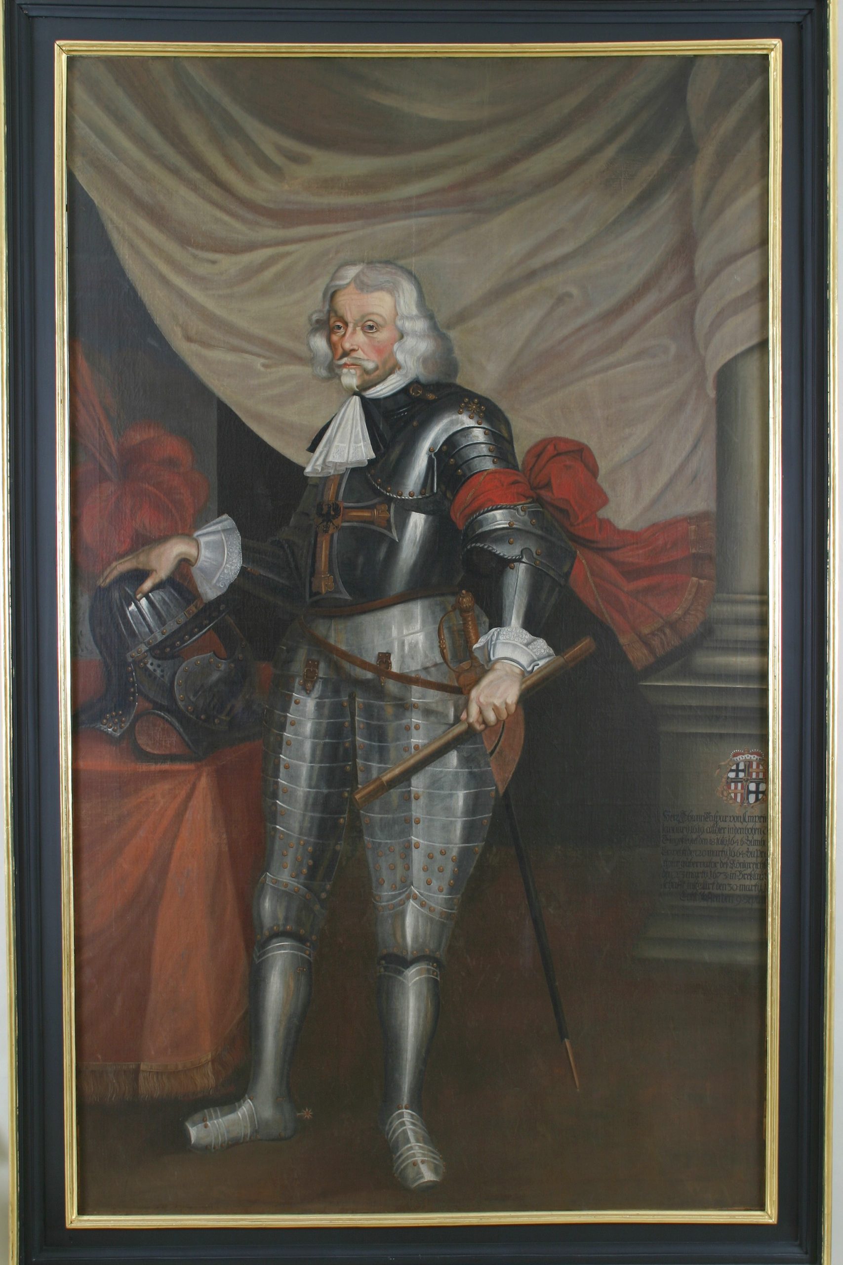 Das Bild zeigt ein Porträt des Hochmeisters Johann Caspar von Ampringen. Er trägt eine Ritterrüstung und hat ein rotes Tuch um den linken Arm gebunden. Neben ihm liegt ein Ritterhelm, auf den er seine rechte Hand stützt.