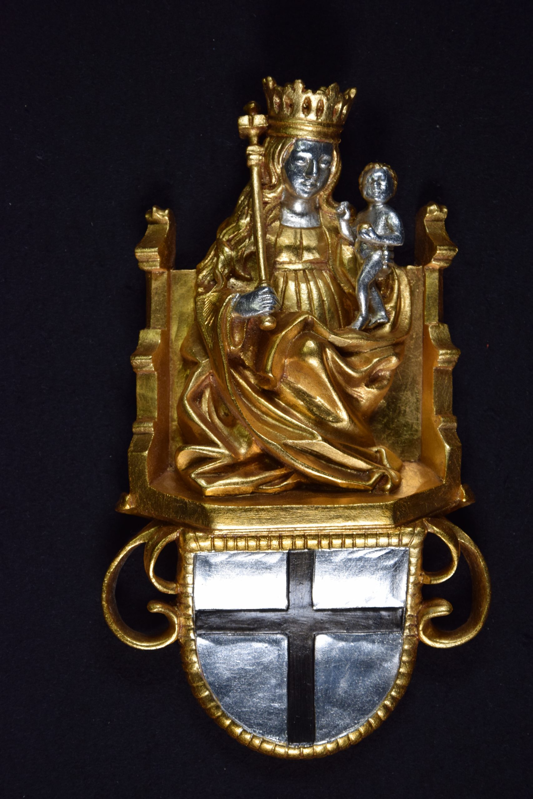 Auf dem Bild ist eine aus vergoldetem Silber abgebildete Marienfigur zu sehen, die auf einem Thron sitzend, mit gekröntem Haupt, Zepter in der rechten Hand und dem Jesuskind auf dem linken Arm dargestellt ist. Unten an der Figur befindet sich das Deutschordenswappen.