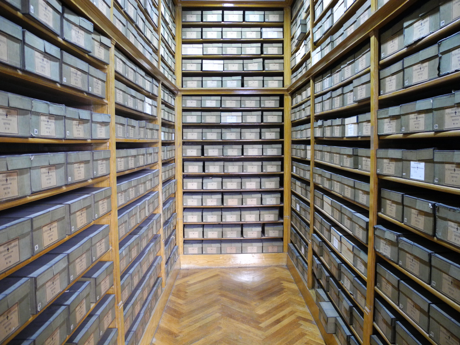 Das Bild zeigt einen Archivalienraum im Deutschordenshaus in Wien, in dem hohe Regale gefüllt mit beschrifteten Kästen zu sehen sind.