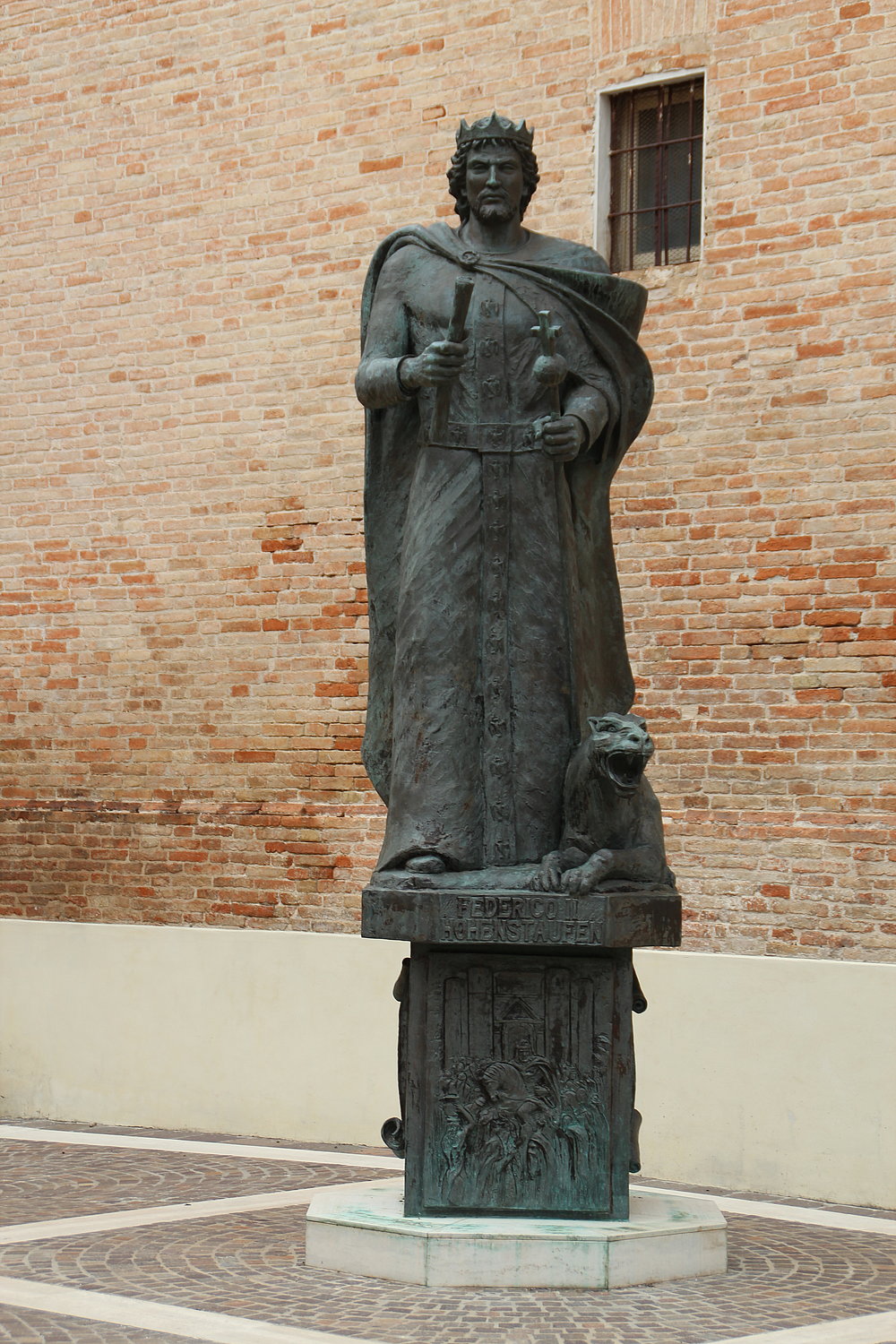 Das Bild zeigt eine Statue von Kaiser Friedrich II., auf einem Sockel stehend und mit Krone auf seinem Haupt. An seiner linken Seite liegt ein Panther.
