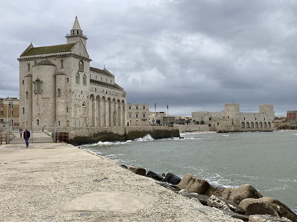 Das Bild zeigt eine seitliche Aufnahme der Kathedrale San Nicola Pellegrino inTrani. Rechts auf dem Bild ist außerdem das Meer zu sehen.