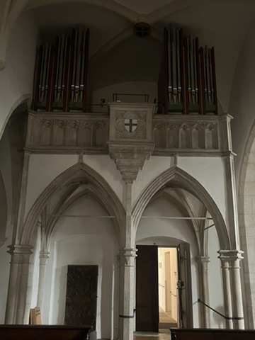 Das Bild zeigt eine Empore in der Deutschordenskirche in Regensburg, auf der die Orgel sowie ein Deutschordenswappen zu sehen ist.