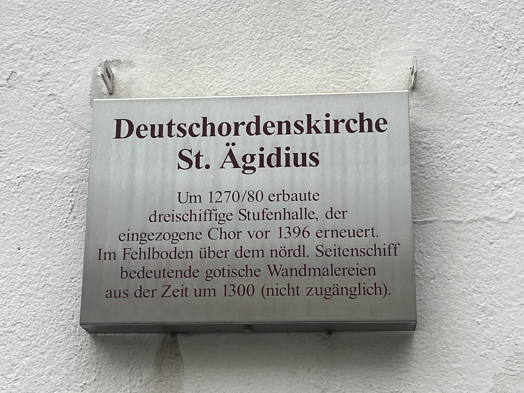 Das Bild zeigt ein Schild, auf dem Informationen zur Deutschordenskirche St. Ägidius in Regensburg stehen.