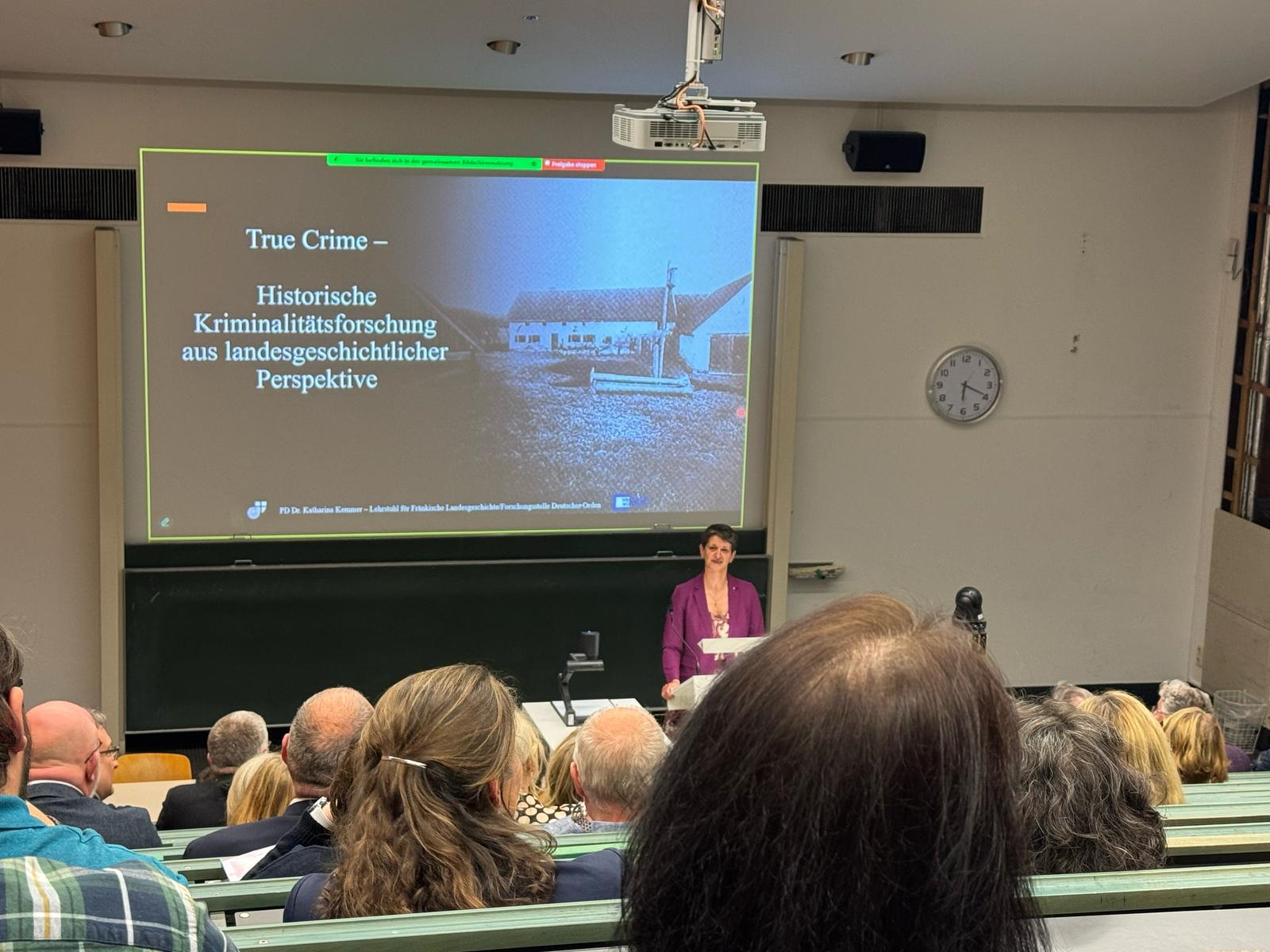 Das Bild zeigt Frau PD Dr. Katharina Kemmer im Hörsaal bei ihrer Antrittsvorlesung zum Thema "True Crime - Historische Kriminalitätsforschung aus langesgeschichtlicher Perspektive".